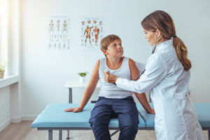 Doctor listening to lungs of preteen patient with asthma