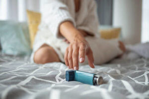 Girl suffering asthma attack reaching inhaler sitting on a bed in the bedroom at home. Woman Hand Reaching Inhaler Because She Suffering From Asthma Attack