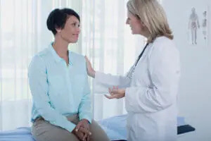 older woman in a blue shirt sitting on an examination table talking to an endocrinologist about her endocrine disorders.