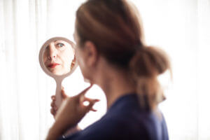 Woman looking in mirror to find relief for rosacea.