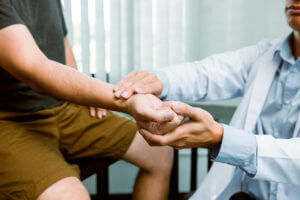 In a clinic room, a physical therapist examines a patient's wrist affected by rheumatoid arthritis by pressing on the wrist bone.