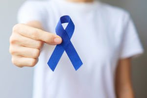 An image representing Colorectal Cancer Awareness Month featuring a woman holding a dark blue ribbon.