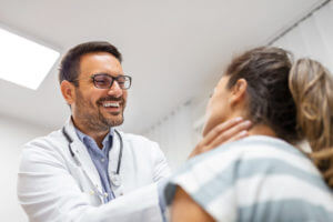 A male endocrinologist is examining the throat of a young woman in the clinic.