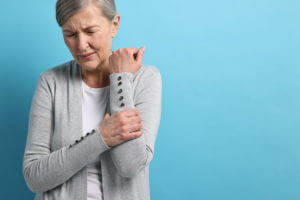 An image depicting a woman experiencing arthritis pain in her arm against a light blue background.