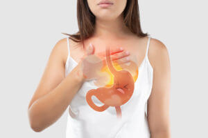 A woman is experiencing symptoms of acid reflux disease while holding her chest.