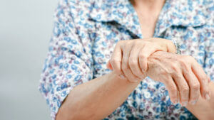 An elderly woman is clutching her wrist in discomfort, suggesting arthritis or mobility issues common in older adults.