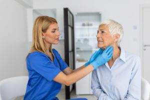 An endocrinologist examining throat of senior woman in clinic.